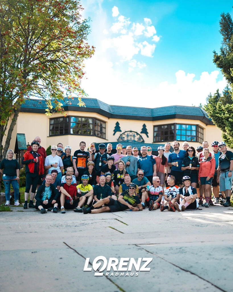 Großes Gruppenfoto aller Radfahrer vor einem Gebäude mit Bäumen im Hintergrund.