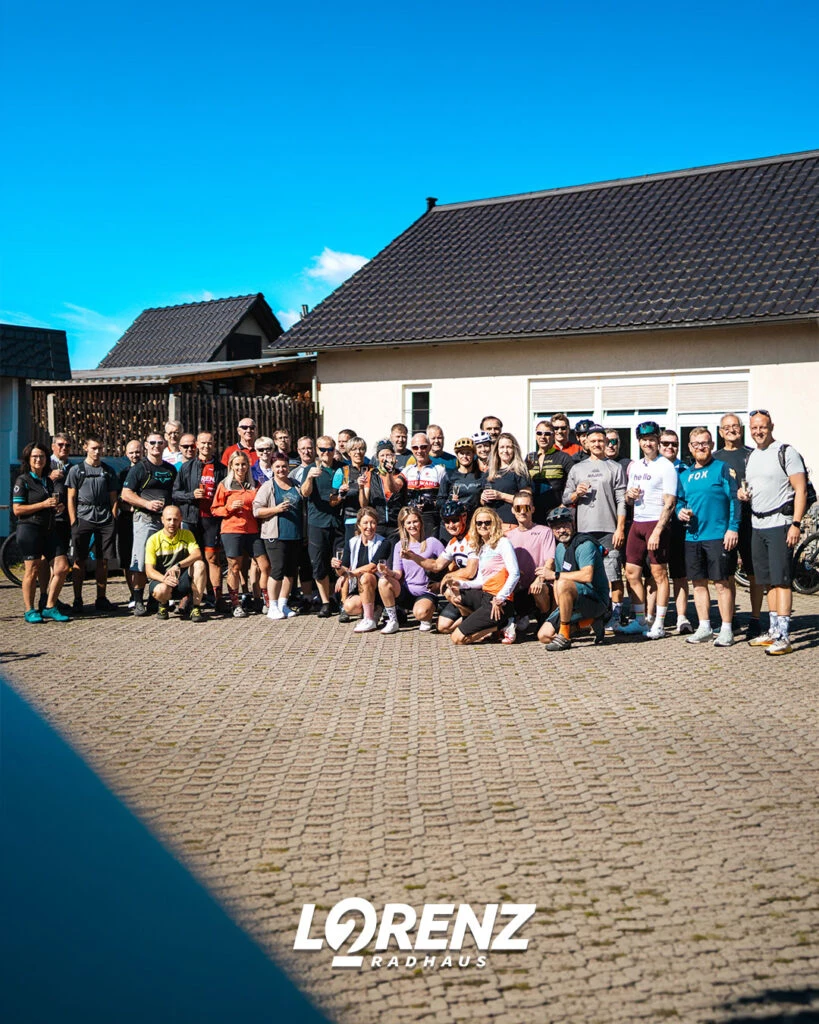Großes Gruppenfoto der Radgruppe auf einem gepflasterten Hof vor einem hellen Gebäude.