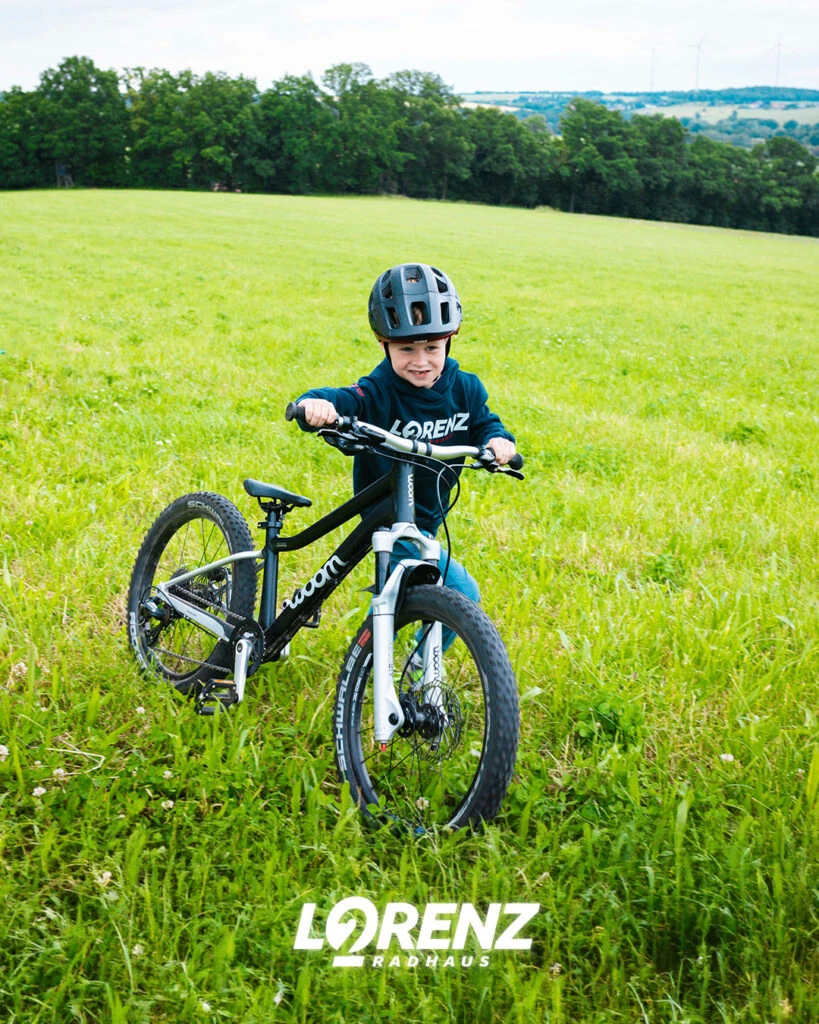 Kleiner Junge schiebt seinKinderrad von Woom über eine Wiese