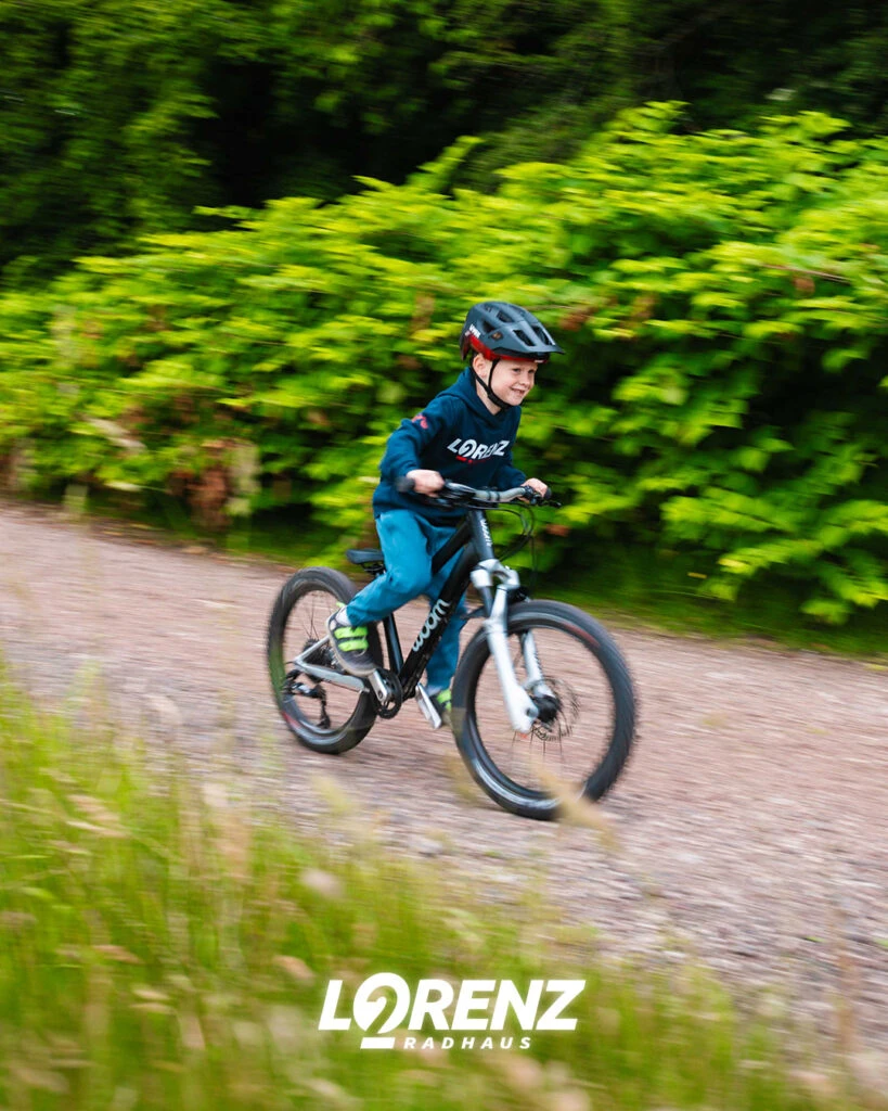 Kleiner Junge mit Held fährt auf einem Woom Kinderrad auf einem Schotterweg